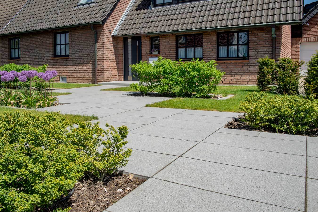 Terrassenplatte METTEN ARCADIA® Cosi in Gartenumgebung mit gepflegtem Rasen und blühenden Pflanzen.