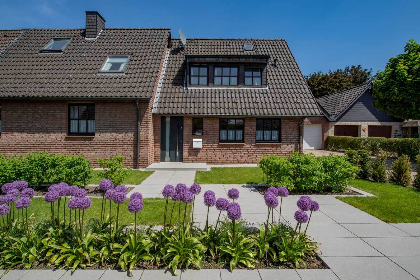 Beautiful home featuring Metten ARCADIA® Cosi concrete patio complemented by vibrant flowers in the garden.