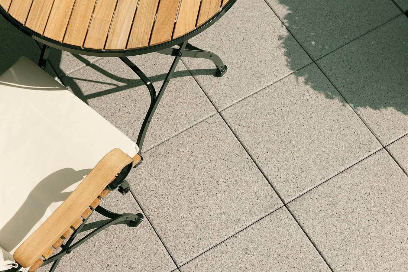 Terrassenplatte METTEN ARCADIA Lugano mit Naturstein-Optik, kombiniert mit Holzstuhl und Tisch im Freien.
