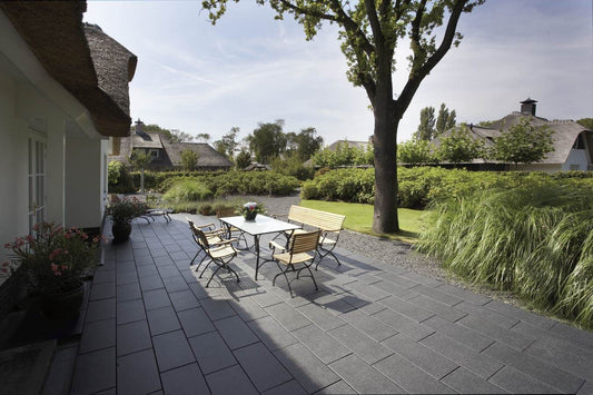 Terrassenbereich mit Metten ARCADIA® Padua Betonplatten, Tisch und Stühlen, umgeben von grünem Garten.