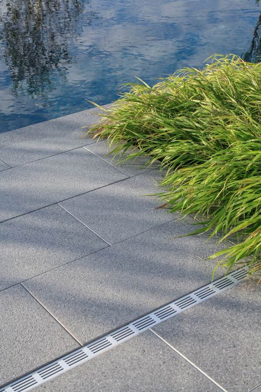 Terrassenplatte METTEN ARCADIA Vivanto in Grau, kombiniert mit Rasen und Wasserbecken.