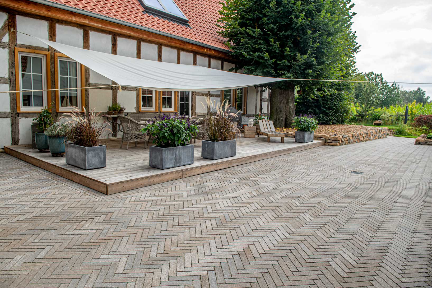 Pflastersteine METTEN SPRING ALVAR Braun-Grau auf einer Terrasse mit Markise und Pflanzenarrangements.