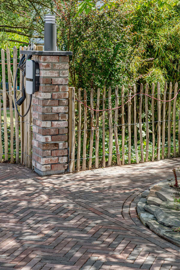 Pflastersteine METTEN SPRING ALVAR Rotschwarz umgeben von einem dekorativen Gartenzaun aus Holz.