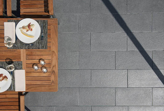 Terrassenplatte METTEN SPRING SORENO Schiefergrau auf einer Terrasse mit Essgeschirr und Holzstühlen.