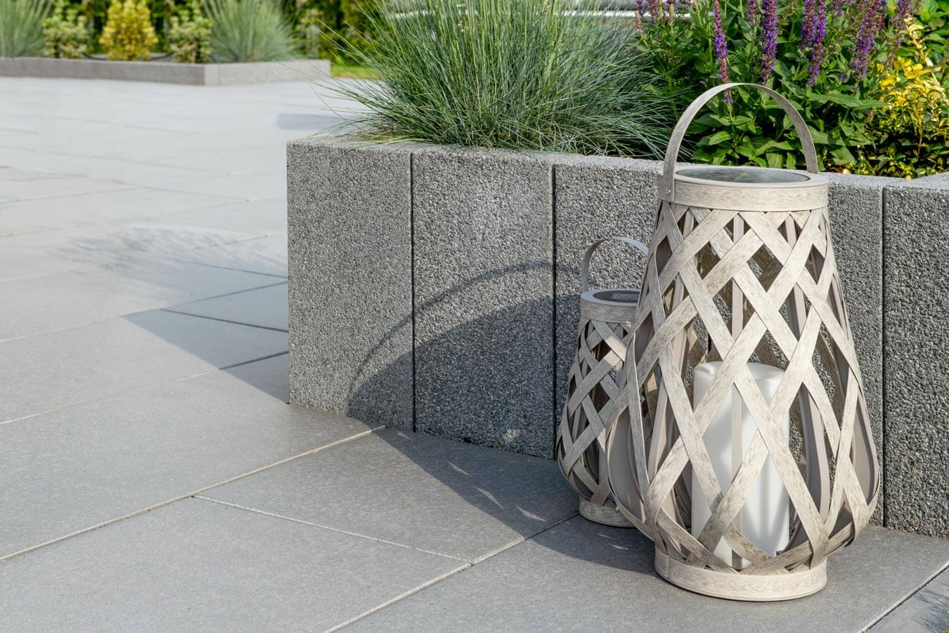 Terrassenplatte METTEN SPRING SORENO Maggiagrau mit dekorativen Laternen im Gartenbereich.