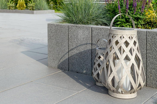 Terrassenplatte METTEN SPRING SORENO Maggiagrau mit dekorativen Laternen im Gartenbereich.