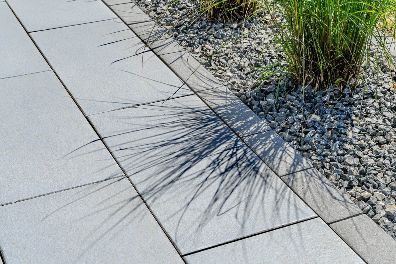 Terrassenplatte METTEN SPRING SORENO Granithell mit Schattenwurf und Gras im Gartenbereich