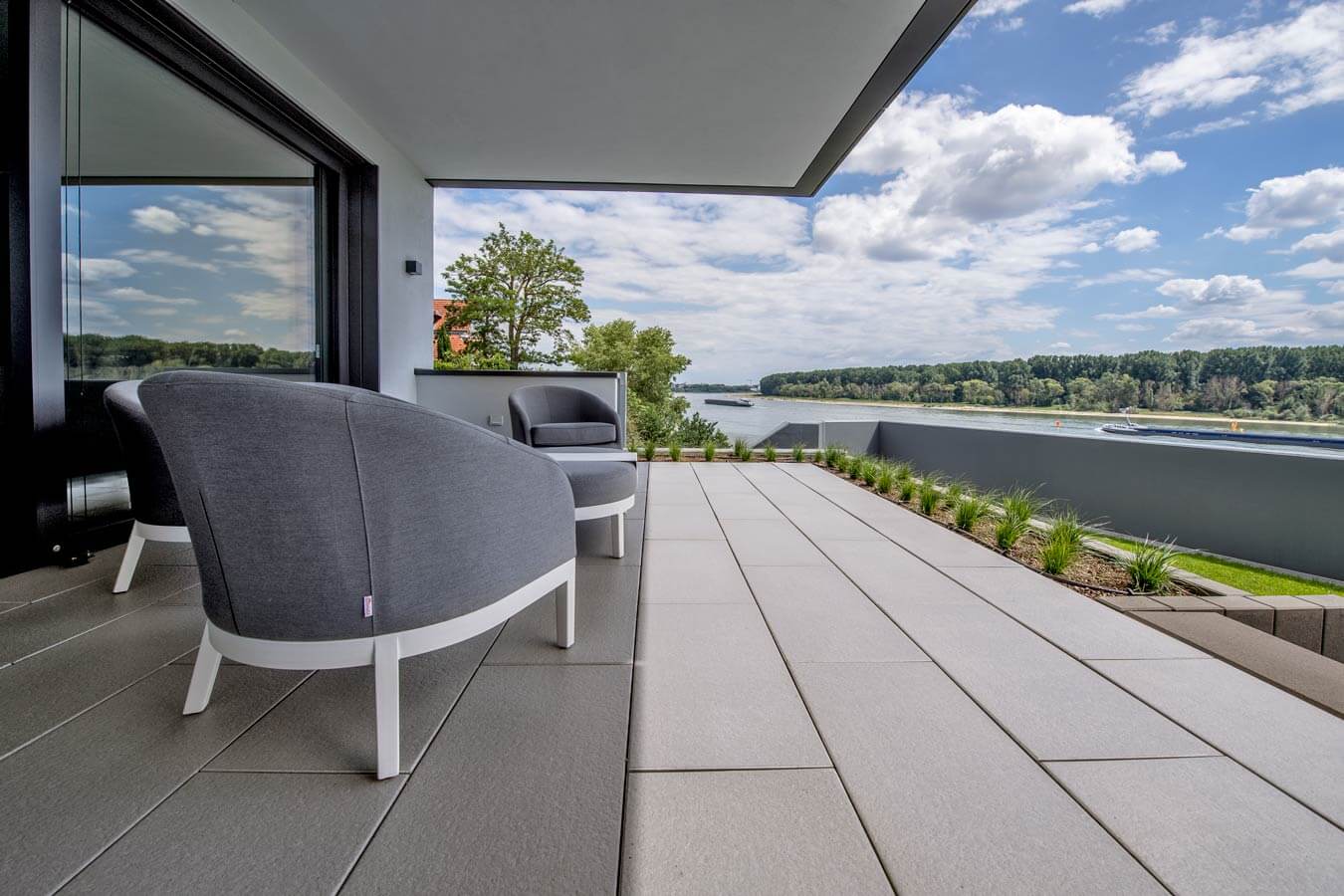 Terrassenplatte METTEN SPRING SORENO Toscanabeige auf einer modernen Terrasse mit Blick auf den Fluss.