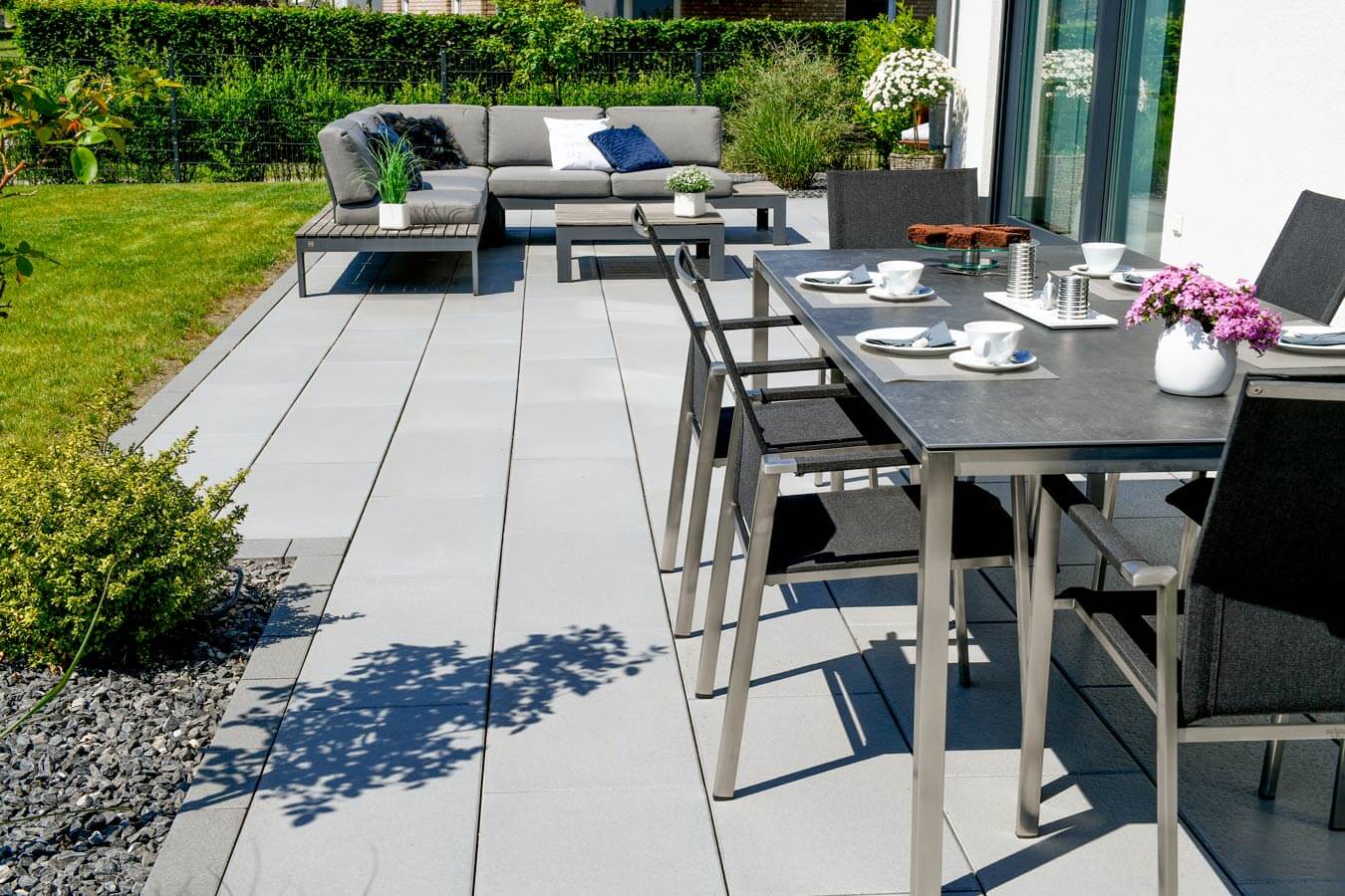 Terrassenplatte METTEN SPRING SORENO Granithell auf einer modernen Terrasse mit Möbeln und Pflanzen.