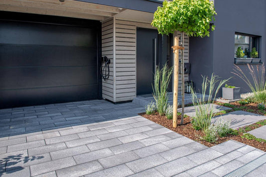 Pflastersteine METTEN UMBRIANO Platingrau am Eingang eines modernen Hauses mit grüner Bepflanzung.