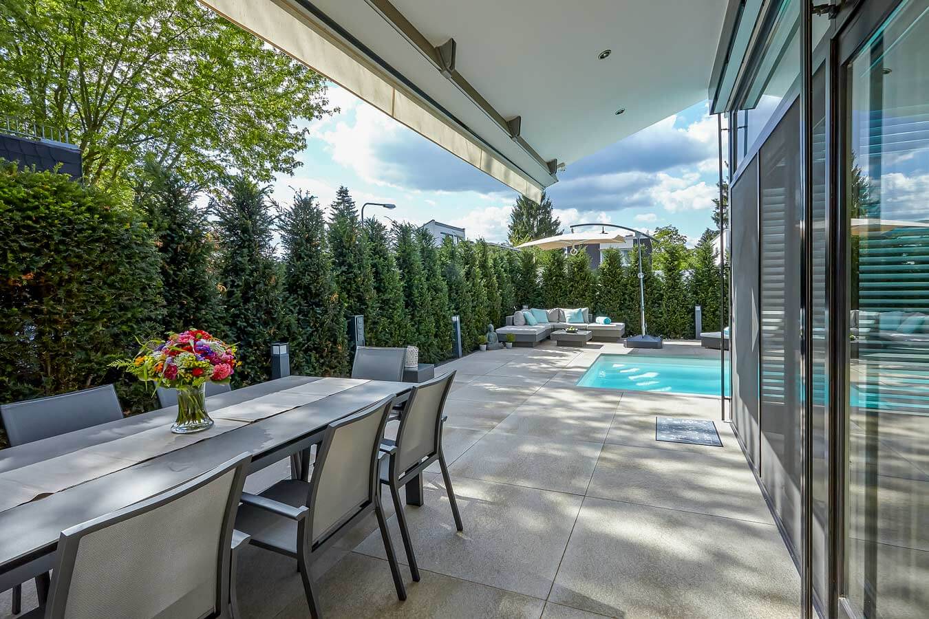 Terrassenplatte METTEN UMBRIANO Granitbeige in modernem Außenbereich mit Pool und Essbereich.