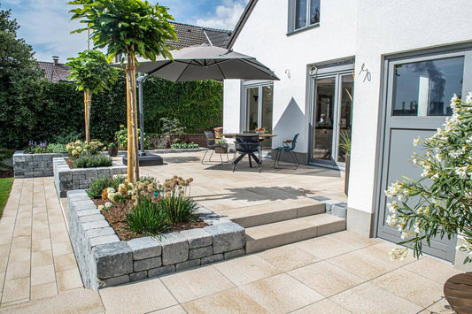 Pflastersteine METTEN UMBRIANO Quarzbeige in moderner Terrasse mit Garten und Sonnenschirm.